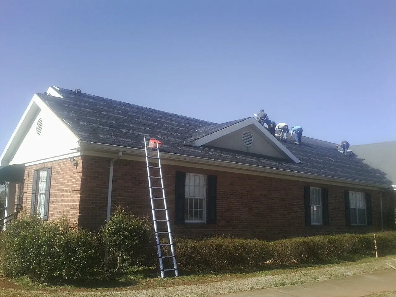 Crew tearing shingles off a brick ranch roof with a ladder set — Metal Roof Repair work by our crew in Canyon Country