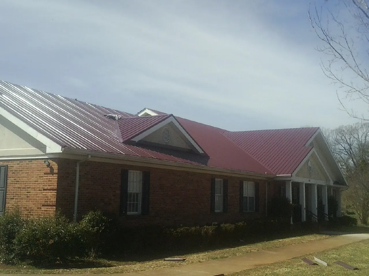 Red metal roof with gabled entries on a long brick building, from a Hail Damage Roof Repair job in Canyon Country
