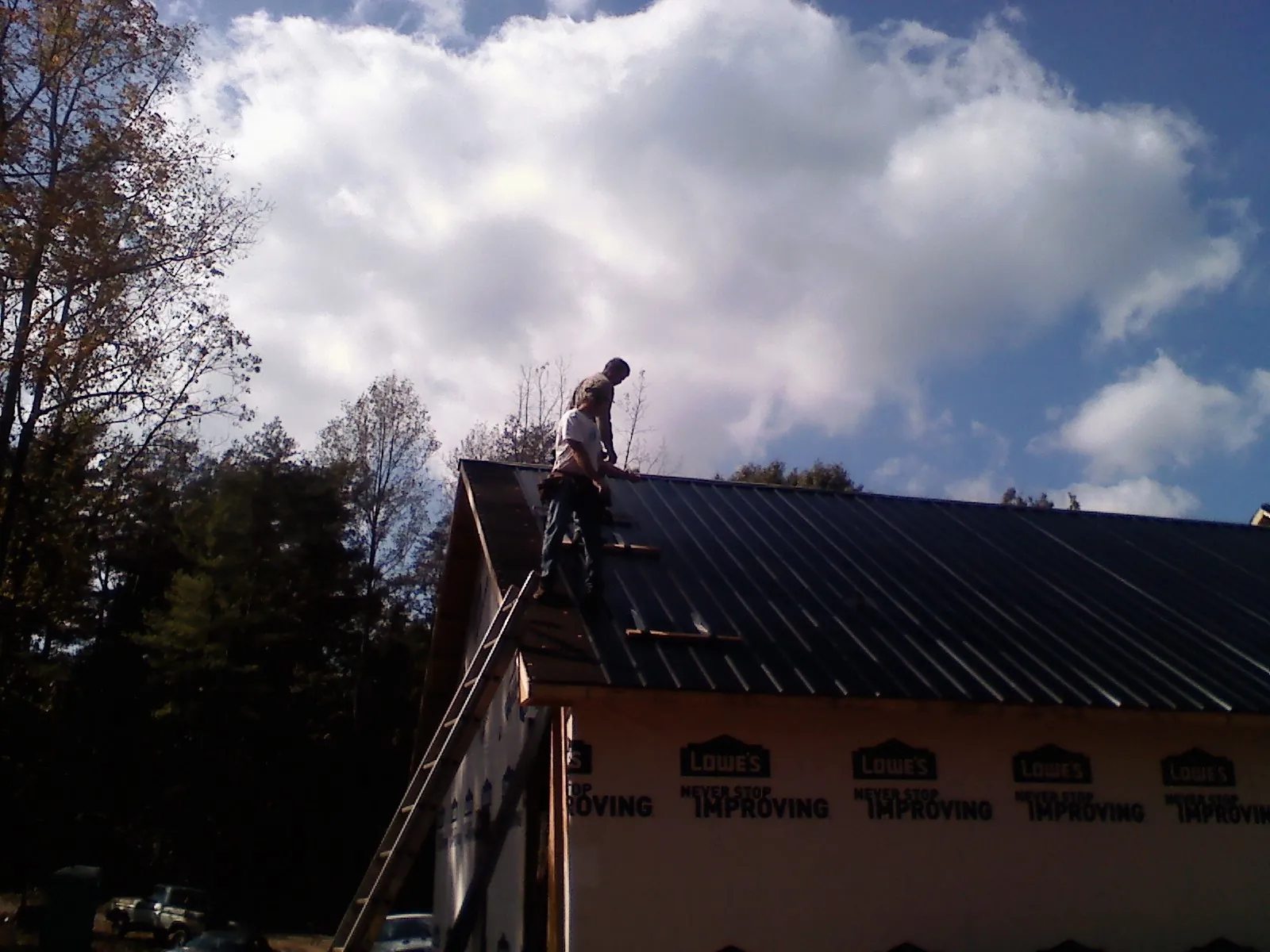 Roofer fastening dark metal panels high against a cloudy sky, from a Roof Inspection job in Canyon Country