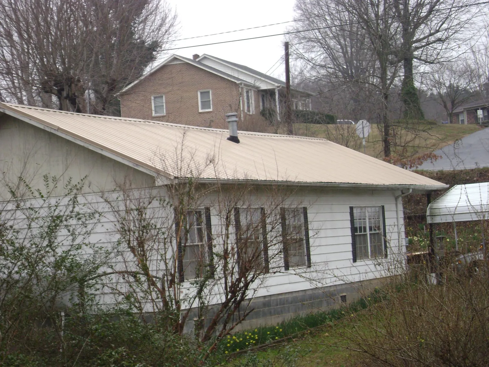 Tan metal roof on a white sided house set into a hillside — Commercial Roofing by Roofing Brothers in Canyon Country